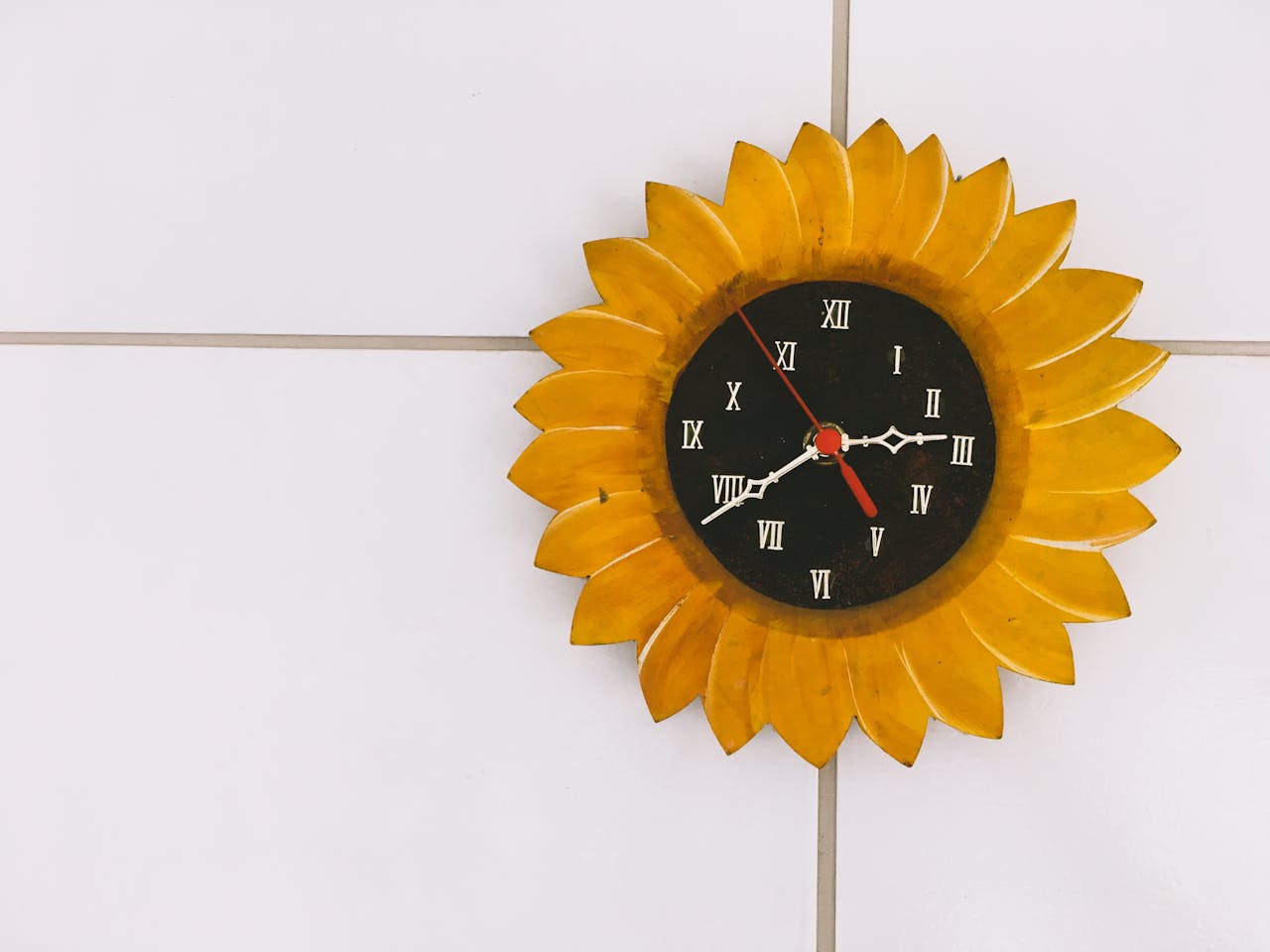 A creative sunflower wall clock with Roman numerals displayed against a tile background.